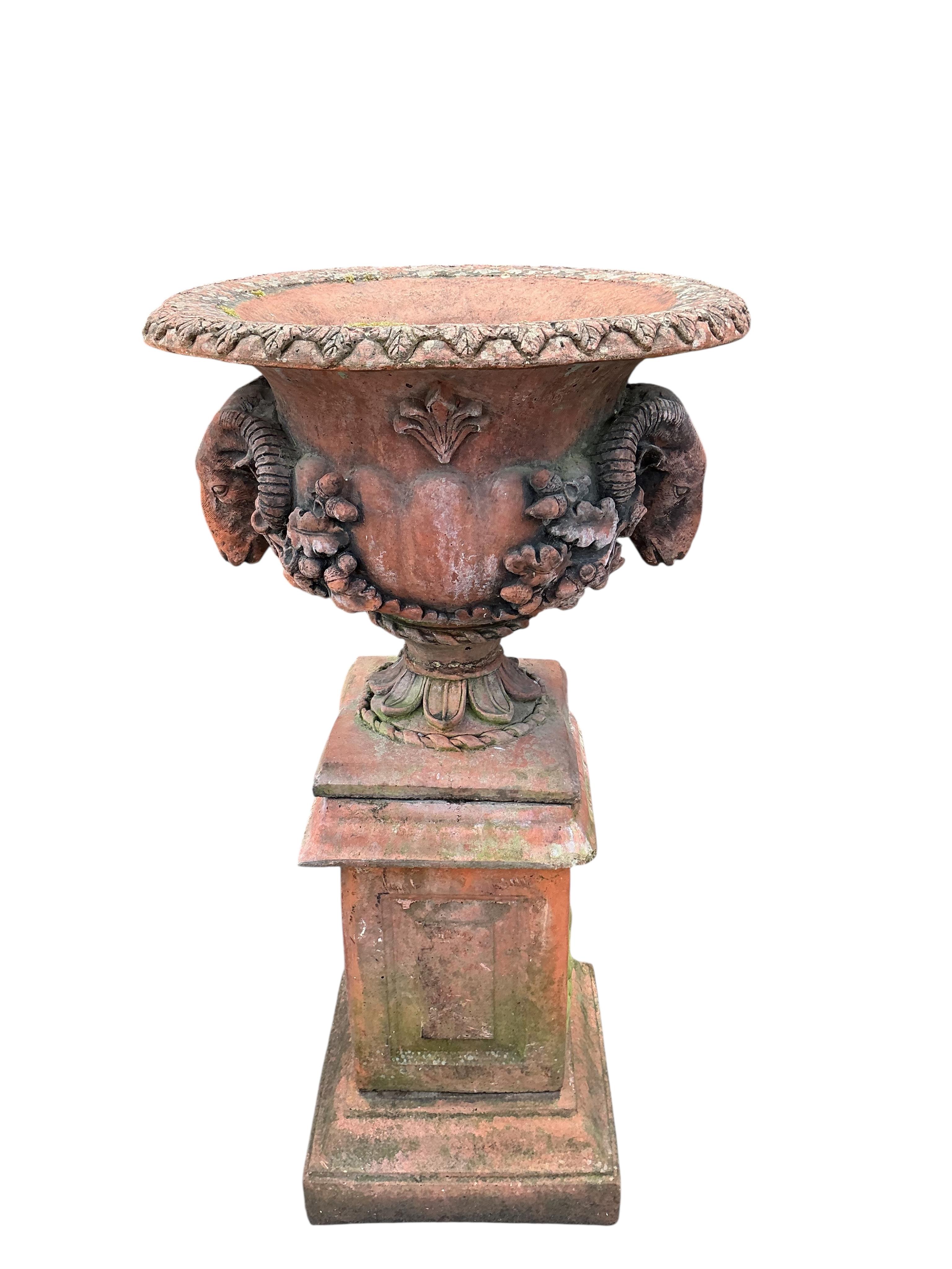 A pair of terracotta ram's head circular garden urns, on square pedestal bases, diameter 52cm, height 98cm